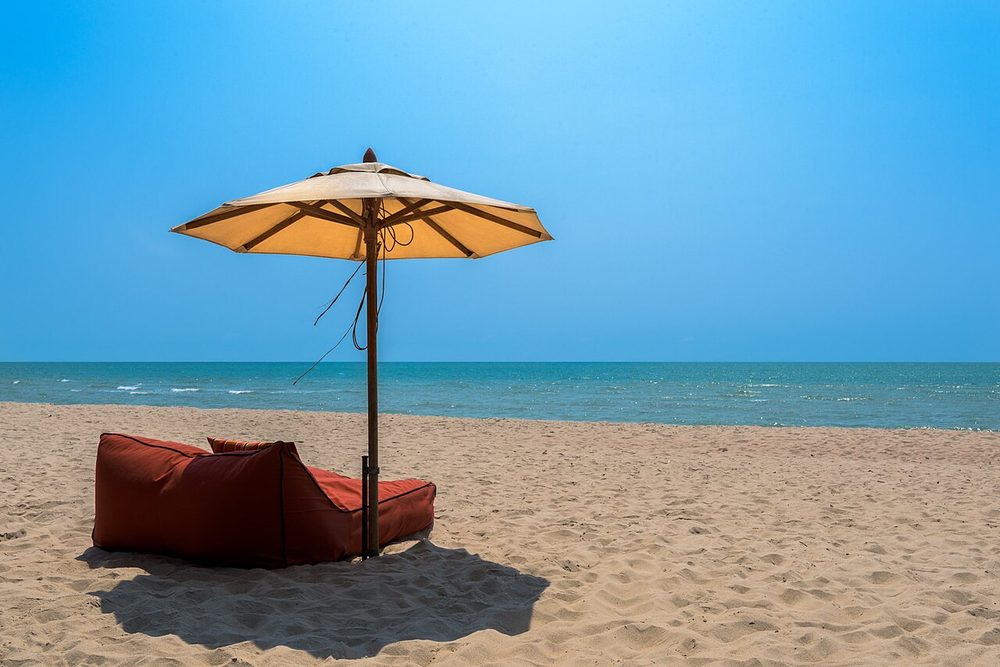 A beach umbrella on sand under a clear blue sky in Thailand